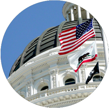 The American flag and State of California flag are raised in front of the Sacramento State Capitol.