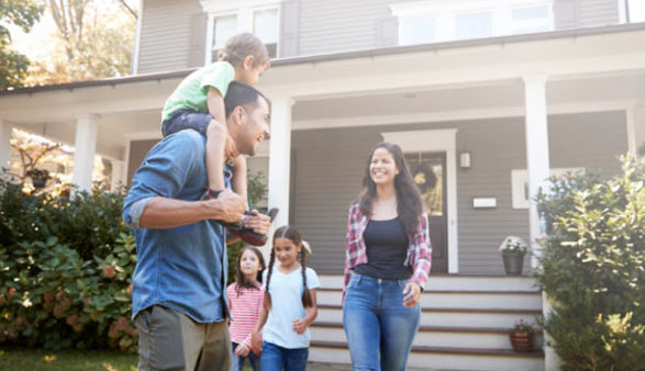 A mixed family with a mom, dad, and 3 kids smile at each other in front of a house.