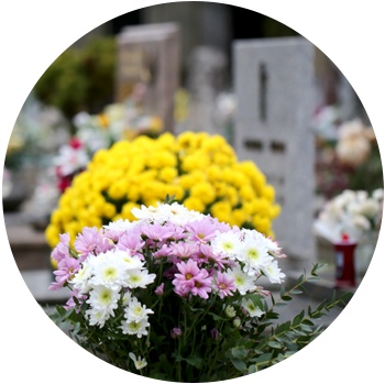 Yellow, white, and purple flowers sit on a grave at a cemetery.