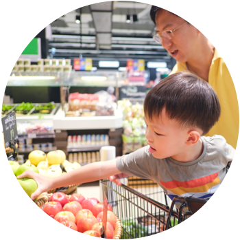 An Asian man is in a grocery store with his young son who sits in a shopping cart.