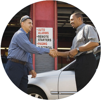 A young man working at an auto repair shop shakes a customer’s hand.