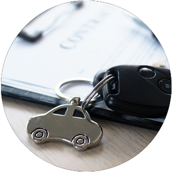 A car key is attached to a car-shaped silver keychain and rests on top of a clipboard.