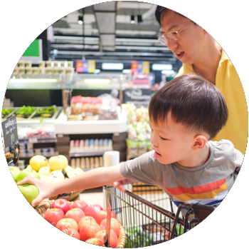 An Asian man is in a grocery store with his young son, who sits in a shopping cart.