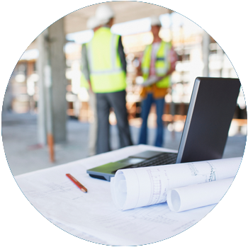 A laptop is on a table with blueprints at a construction site.