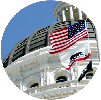 The American flag and State of California flag are raised in front of the Sacramento State Capitol.