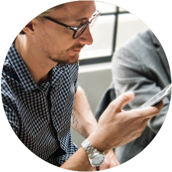 A young white man with glasses sits and looks at his phone.