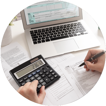 A person with light-skinned hands uses a calculator and fills out tax forms in front of a laptop.