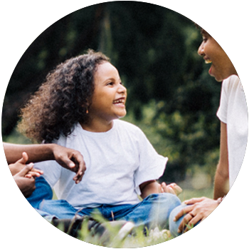 A young Black girl with curly hair smiles at her mom and holds hands with her father in a field.